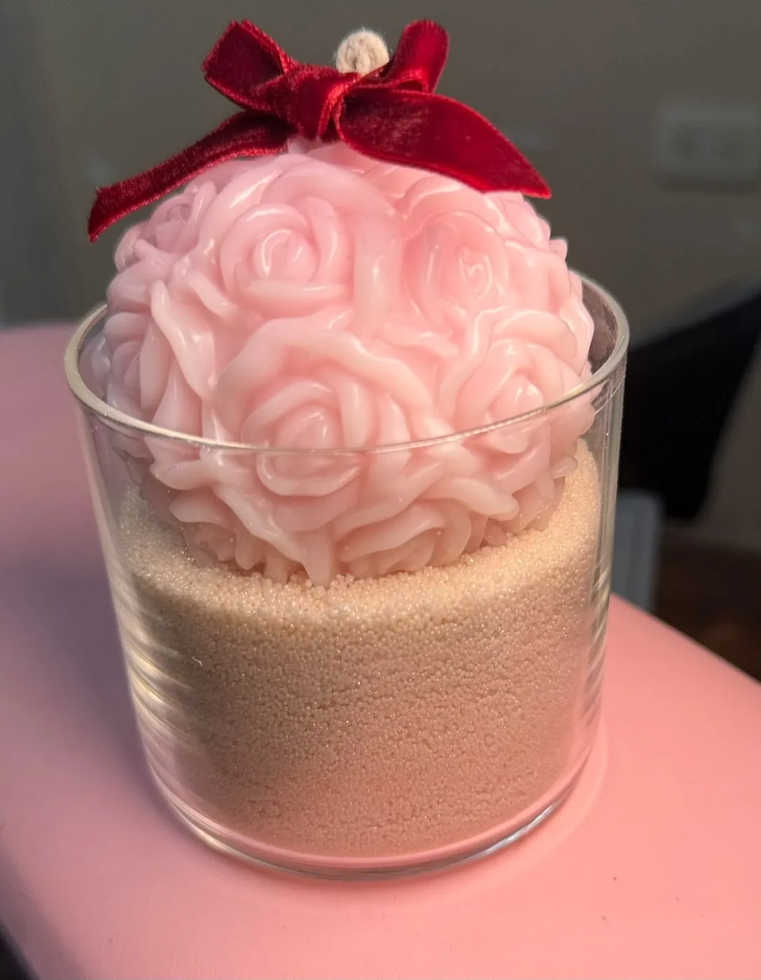 Vela bola de rosas sobre arena en vaso de vidrio con moño vino